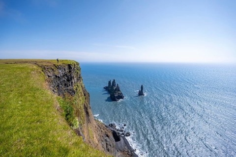 Young man standing on cliff, view from steep cliff to the rocks Reynisdrangar in the water, at