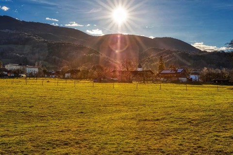 The sun sets over a village that lies in front of a mountain range and is surrounded by green