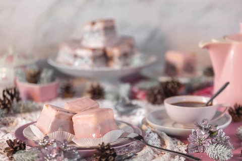 Pink glazed cakes, punch doughnuts surrounded by winter decorations, coffee pot and cup of coffee