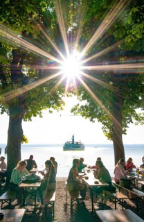 People in a beer garden under chestnut trees in Herrsching am Lake Ammer, in the background a