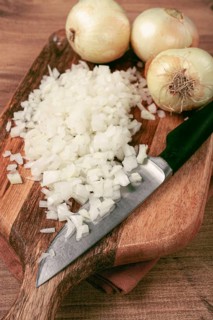 Finely chopped onion on a chopping board with a knife, wooden table, top view, no people