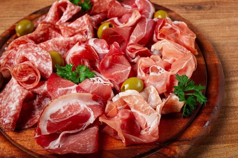 Assortment, sliced meat appetizer, prosciutto, salami and ham, with olives, on a wooden board,