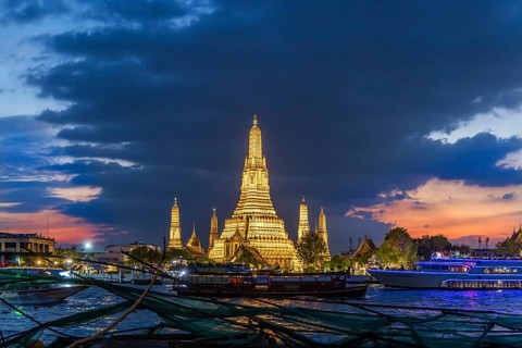 Wat Arun, Temple of Dawn at sunset with dark clouds. Boats on the Chao Phraya river. Tourist