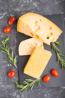 Various types of cheese with rosemary and tomatoes on black slate board on a black concrete