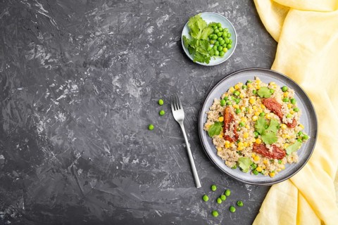 Quinoa porridge with green pea, corn and dried tomatoes on ceramic plate on a gray concrete
