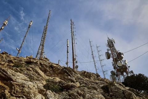 Several radio masts and antennas towering into the cloudy sky on a rocky hill, mountain top,