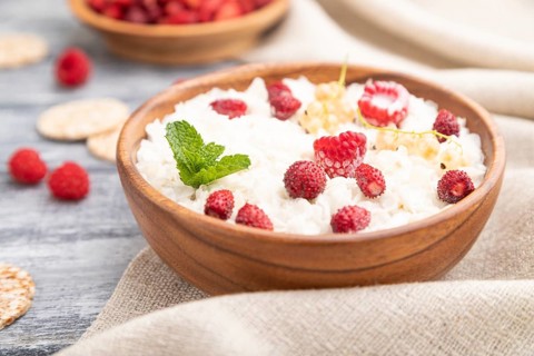 Rice flakes porridge with milk and strawberry in wooden bowl on gray wooden background and linen