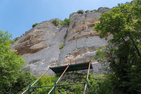 Scaffolding in front of a high rock face surrounded by trees and blue sky, rock relief, Horsemen of