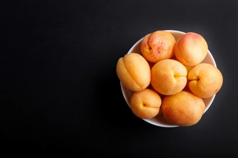 Fresh orange apricots in white bowl on black background. top view, flat lay, copy space