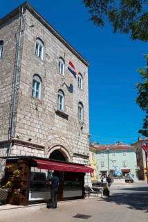 Tall stone building with characteristic windows and a flag, surrounded by trees and a clear blue