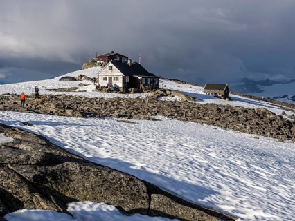 Mountain hut on top of mountain Fannaråken, hikers sit outside the hut, enjoy the sun, Jotunheimen
