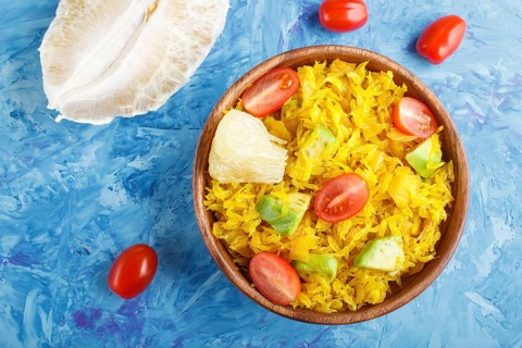 Fried pomelo with tomatoes and avocado in wooden plate on blue concrete background. Top view,