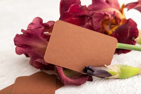 Brown business card with iris burgundy purple flowers on white concrete background. side view, copy
