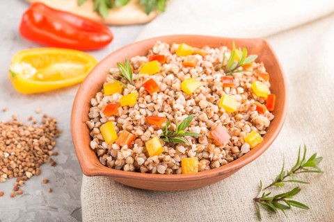Buckwheat porridge with vegetables in clay bowl on a gray concrete background and linen textile.