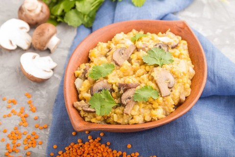Lentils porridge with champignons and coriander in a clay bowl on a gray concrete background and