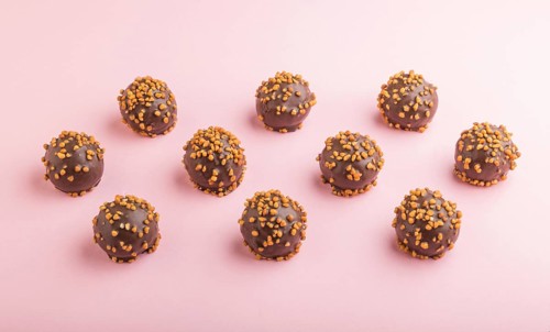 Chocolate caramel ball candies with almonds in a row on a pastel pink background. side view, close