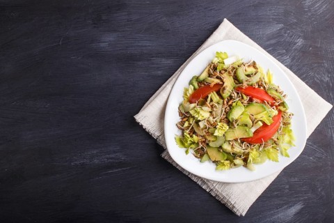 Vegetarian salad of celery, germinated rye, tomatoes and avocado on linen tablecloth, top view,
