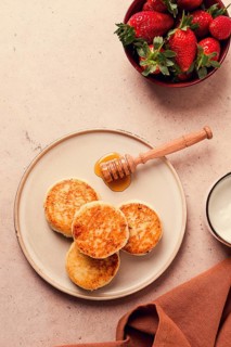 Cottage cheese pancakes with white sauce and strawberries, on a beige table, top view, selective