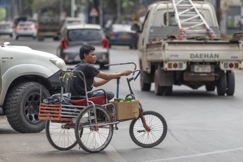 Man with an amputated leg on a hand-propelled tricycle, road traffic in Vientiane, Laos, Asia