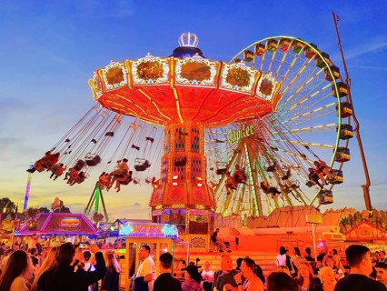 The colourfully illuminated Wellenflug chain carousel and the Ferris wheel in the evening, Cranger