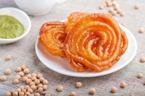 Traditional indian candy jalebi in white plate with mint chutney on a gray concrete background.