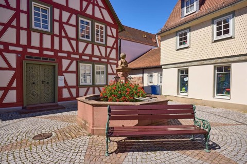 Running fountain with flowering geraniums and bench in Michelstadt, Odenwald, Odenwaldkreis, Hesse,