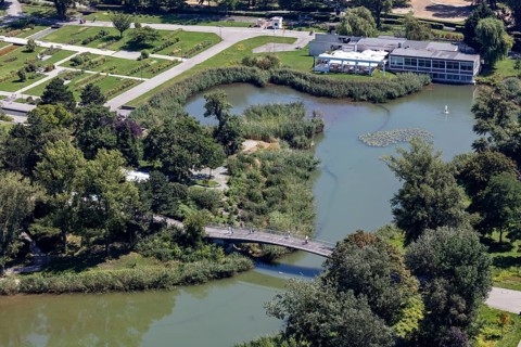 A green park with a bridge and river surrounded by lush vegetation, Vienna