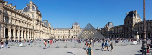 Sweeping view of the Louvre with the striking pyramid and many visitors on a sunny day, Paris
