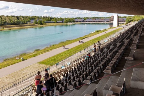 Perspective from grandstands on a lake with sporting activities and green surroundings,
