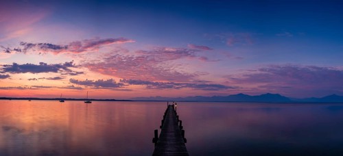Panoramic photo, Illuminated clouds over sailing boats and jetty on Lake Chiemsee at dawn, behind