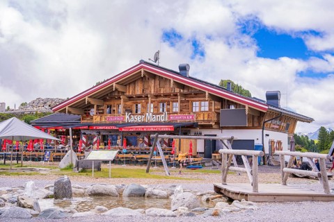 A rustic Alpine restaurant with wooden beams and outdoor seating against a mountain backdrop,