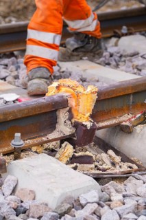 Close-up of a damaged section of track with a construction worker dressed in orange in the