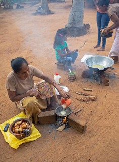 Sri Lankan woman, 63 years old, frying traditional doughnuts on a fire on the ground, Sella