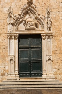 Ornate dark green entrance door decorated with carved religious figures at Franciscan Monastery,