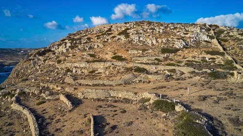 Drone image, Archaeological excavation site, A rocky hill under blue sky with visible dry stone