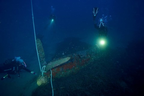 Divers illuminate an aircraft wreck from the Second World War during an underwater exploration,