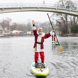 Water sports enthusiasts dressed as Santas ride SUPs on the Spree in front of the Insel der Jugend