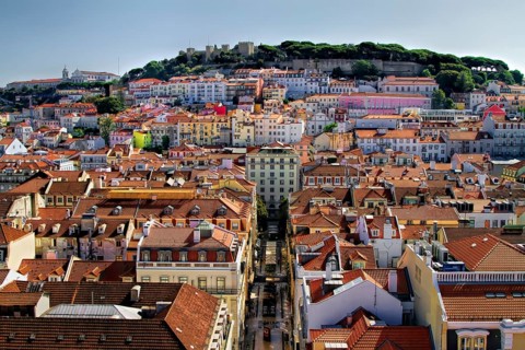 Sunlit cityscape with colorful buildings and a castle atop a hill, Alfama, Lisbon