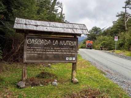 Information board at waterfall Cascada La Nutria, overlander truck on gravel road, Valle