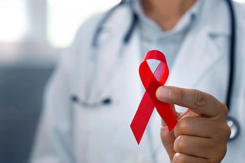Red AIDS awareness ribbon held by doctor's hand. Generative AI, AI generated