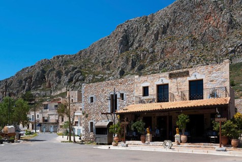 A Mediterranean village with stone buildings in front of a rocky mountain landscape under a clear