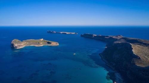 Drone shot, panoramic view of two islands, one with green vegetation and one rocky, surrounded by