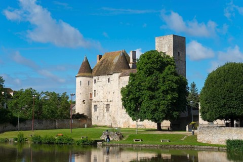 Historisches Schloss mit Burgturm an einem klaren blauen Himmel, umgeben von grünen Bäumen und