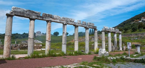 Column ruins on a green meadow in front of a partly cloudy blue sky in a historical site, Messene,