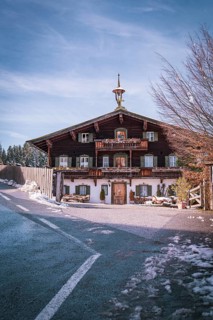 Traditional Bavarian country house on a snow-covered road under a clear blue sky, Der Bergdoktor