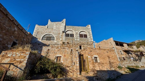 A medieval stone castle built on a hill, under a clear blue sky, Vathia, residential tower village,