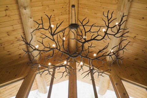 Illuminated deer antlers chandelier hanging from high cathedral knotty pine wood planks ceiling
