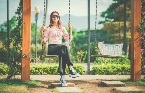 Cheerful girl in glasses relaxing on a swing in a natural park. Happy young woman sitting on a