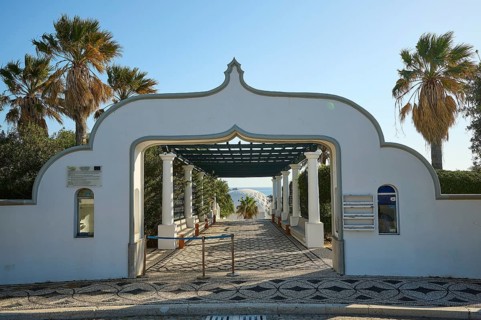 Decorative entrance gate in a white building, surrounded by palm trees, overlooking a sunny sea,