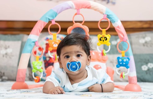 Baby boy playing lying on bed with pacifier on mouth